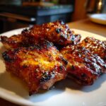 Close-up of juicy Baked Honey Garlic Chicken pieces on a white plate, glistening with sauce and herbs.