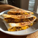 Close-up of three golden-brown Beef Quesadillas stacked on a white plate, filled with seasoned ground beef and melted cheese.
