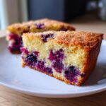 A rustic slice of blackberry cornmeal cake with visible whole blackberries and a sugar-sprinkled crust.