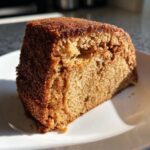 A close-up of a moist slice of Chai Spice Cake on a white plate, showcasing its warm brown color and fluffy texture.