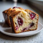 A close-up of a slice of Cherry Almond Ricotta Cake, showing moist cake with whole cherries baked inside.