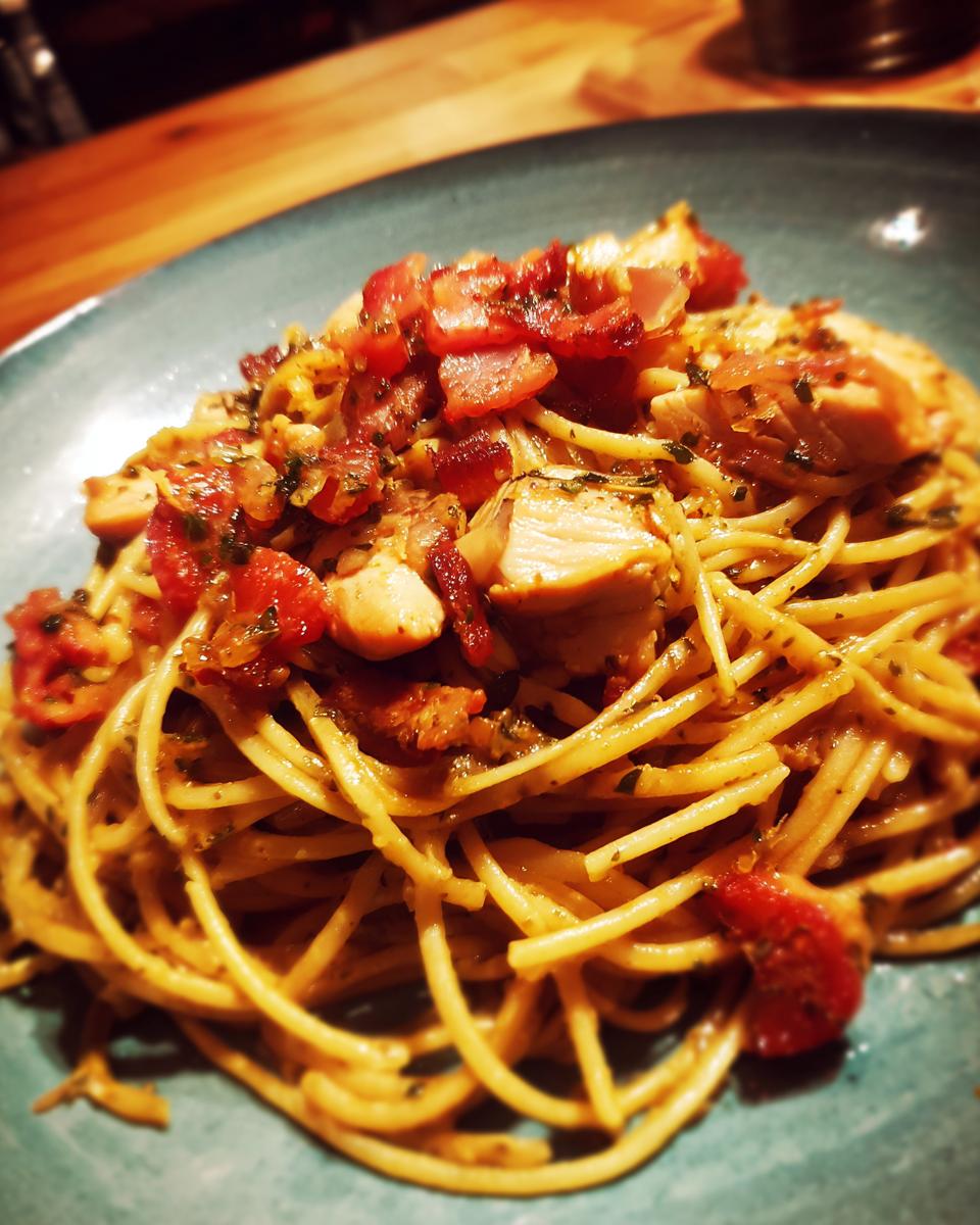 A close-up of a plate of Chicken and Bacon Pasta, featuring spaghetti topped with chicken pieces, crispy bacon, and diced tomatoes.