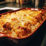 A close-up, angled view of a golden-brown Chicken and Rice Casserole baked in a red rectangular dish, topped with melted cheese.