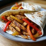 Close-up of a chicken fajita wrap filled with seasoned chicken strips, red and yellow bell peppers, and onions.