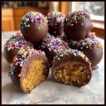 A close-up of chocolate cake pops covered in colorful sprinkles, with one cut in half to reveal the cakey interior.