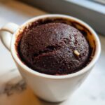 A close-up of a freshly baked chocolate mug cake in a white mug, perfect for a quick dessert.