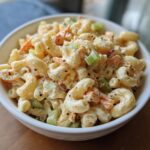 A close-up of a bowl of classic macaroni salad with elbow pasta, celery, carrots, and a creamy dressing.