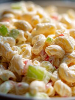 A close-up, creamy shot of classic macaroni salad with visible pieces of celery and red pepper.