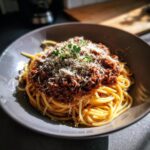 A close-up of a bowl filled with Classic Spaghetti Bolognese, topped with rich meat sauce, grated Parmesan cheese, and fresh parsley.