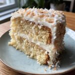 A generous slice of Coconut Layer Cake with fluffy white frosting and toasted coconut flakes.