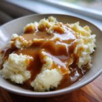 A close-up of creamy mashed potatoes generously topped with rich, brown gravy, perfect for a holiday meal.