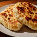 Close-up of two golden-brown, puffed Easy Pita Bread on a white plate, with some charred spots.