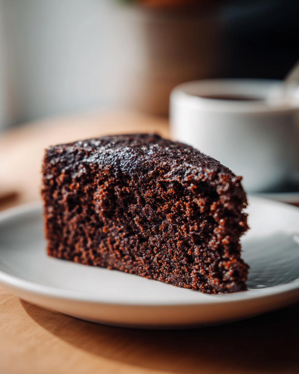 A close-up of a slice of rich, dark Ginger Molasses Cake on a white plate.