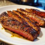 Close-up of perfectly grilled flank steak with marinade, sliced and served on a white plate.