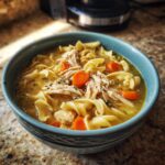 A comforting bowl of Homemade Chicken Noodle Soup Holiday, featuring shredded chicken, wide egg noodles, and sliced carrots.