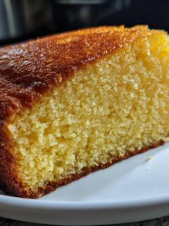 A close-up of a slice of homestyle yellow cake on a white plate, showing its golden-brown crust and moist crumb.