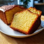 Two moist slices of homestyle yellow cake with a golden crust, served on a white plate.