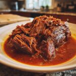 Close-up of shredded Italian Pot Roast Stracotto in a rich, red sauce on a white plate.