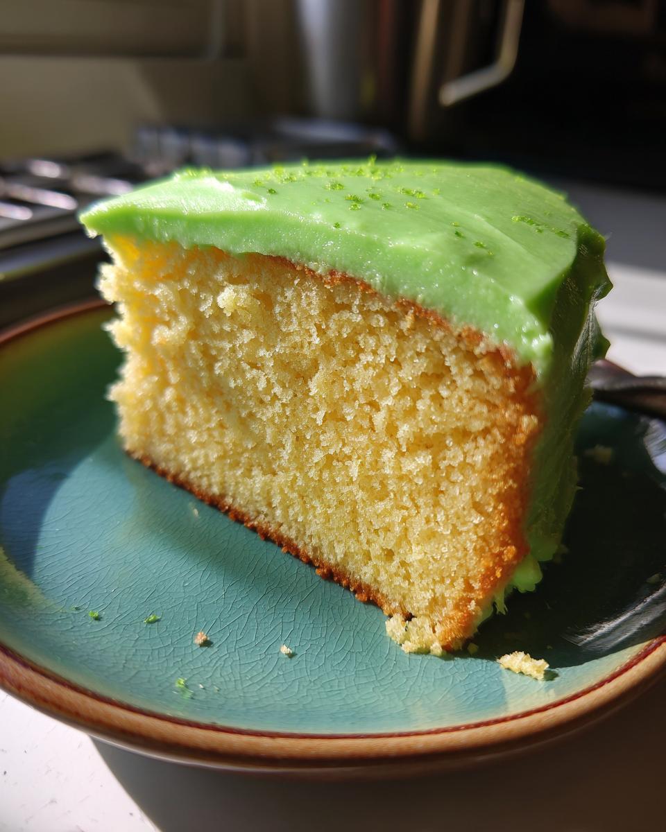 A close-up of a slice of Key Lime Cake, featuring a vibrant green frosting and a fluffy yellow cake crumb.