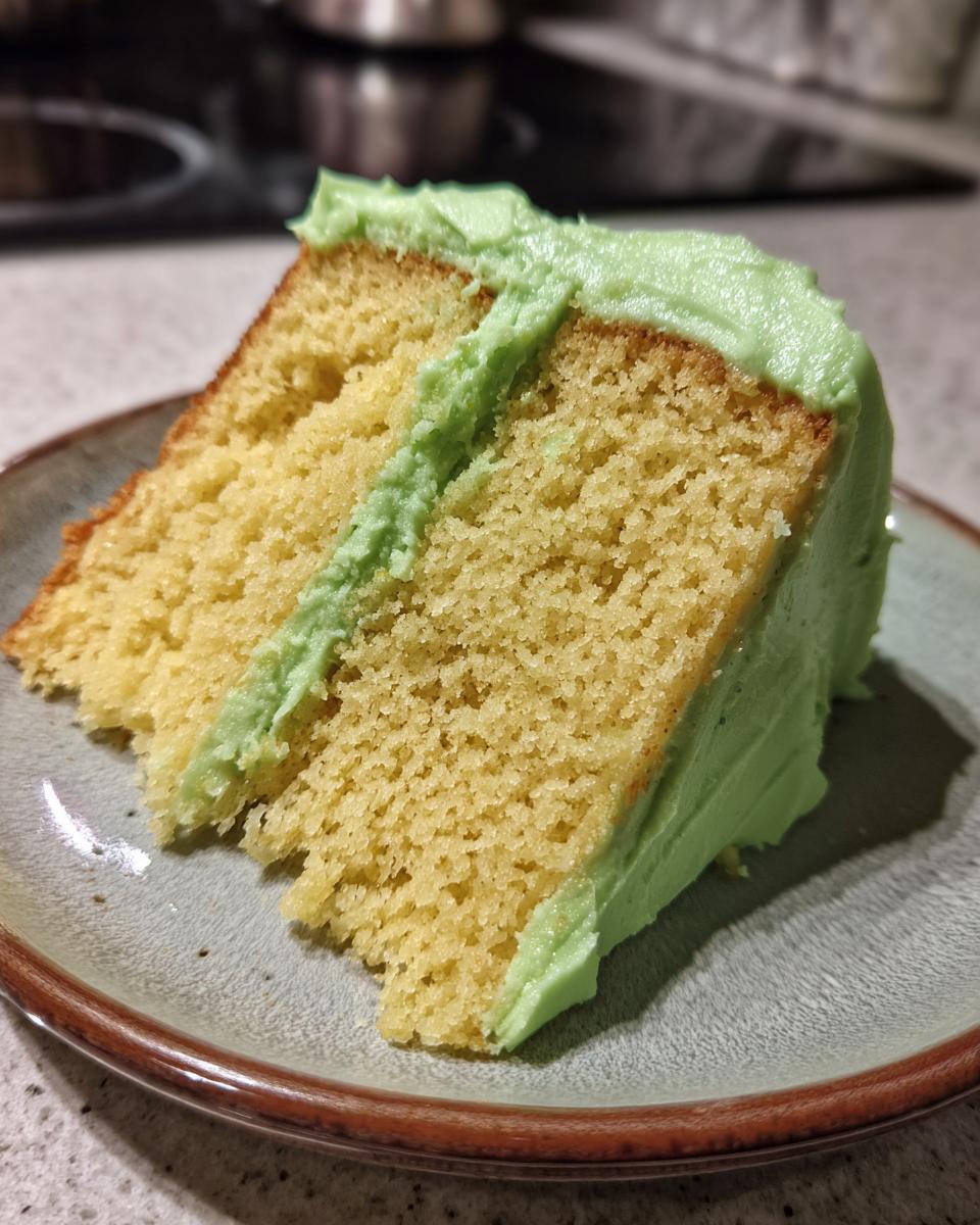 A close-up of a moist slice of Key Lime Cake with vibrant green frosting.