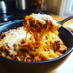 A fork lifts a cheesy, saucy portion of Lasagna Soup from a dark bowl.