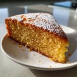 A moist slice of delicious Lemon Cake, dusted with powdered sugar, served on a white plate.