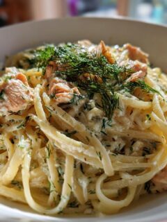 Close-up of a bowl of creamy Lemon Dill Salmon Pasta topped with fresh dill.