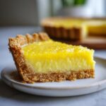 A close-up of a slice of Lemon Icebox Pie on a plate, showcasing its creamy filling and crumb crust.