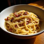 A close-up of a bowl of Pasta Carbonara, featuring spaghetti, crispy bacon, and grated cheese.