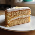 A slice of Pineapple Cream Cake with fluffy white frosting and a pineapple filling, served on a white plate.