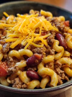 A close-up of a bowl filled with Quick Chili Mac With Ground Beef, topped with shredded cheese.