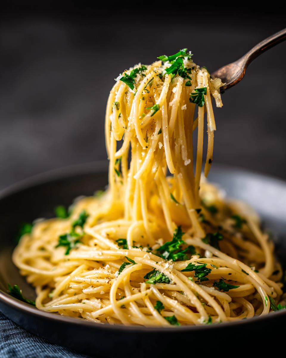 A fork twirls a portion of Spaghetti Aglio e Olio, garnished with fresh parsley and grated cheese.