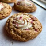 Close-up of a delicious Strawberry Cheesecake Cookie topped with creamy frosting and pink strawberry crumbles.