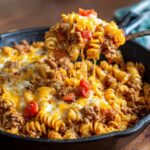 A spoonful of cheesy Taco Mac Skillet with ground beef, pasta, and tomatoes, showing melted cheese strings.