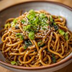 A close-up, appetizing shot of glossy, saucy noodles creating a perfect Noodles Aesthetic, topped with sesame seeds and green onions.