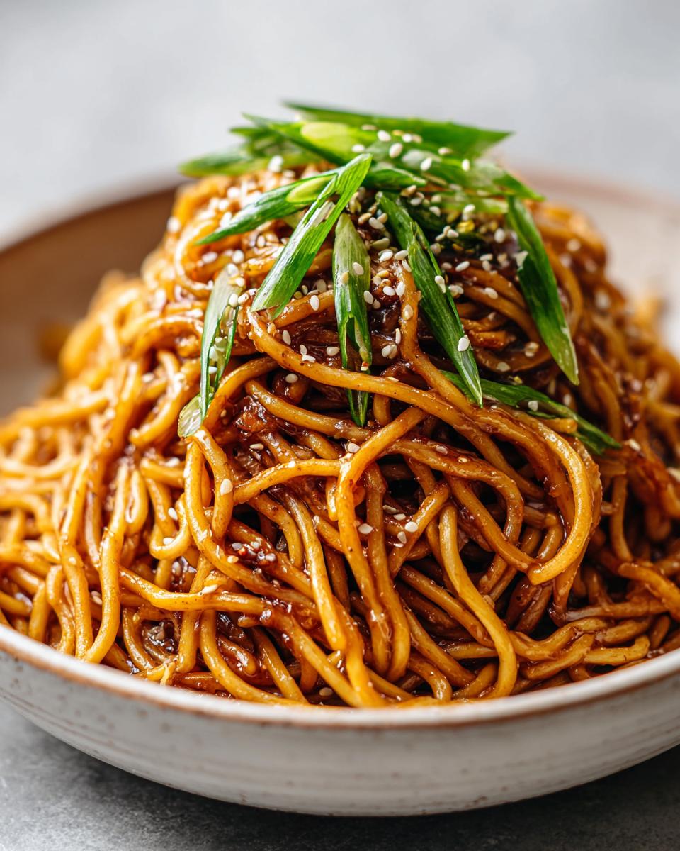 Close-up of glossy, saucy noodles piled high, showcasing the Noodles Aesthetic, topped with green onions and sesame seeds.