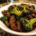 A close-up shot of tender beef slices and bright green broccoli florets coated in a rich, dark sauce, ready to serve for Beef And Broccoli Stir Fry.