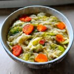A close-up of a bowl filled with vibrant Cabbage Soup featuring large pieces of cooked cabbage and bright orange carrot slices.
