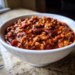Close-up of a white bowl filled with rich, thick Chicken Chili featuring ground meat and kidney beans.