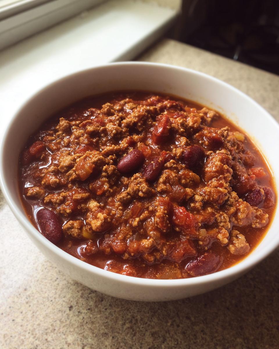 Close-up of a white bowl filled with rich, savory Chicken Chili featuring ground meat and kidney beans.