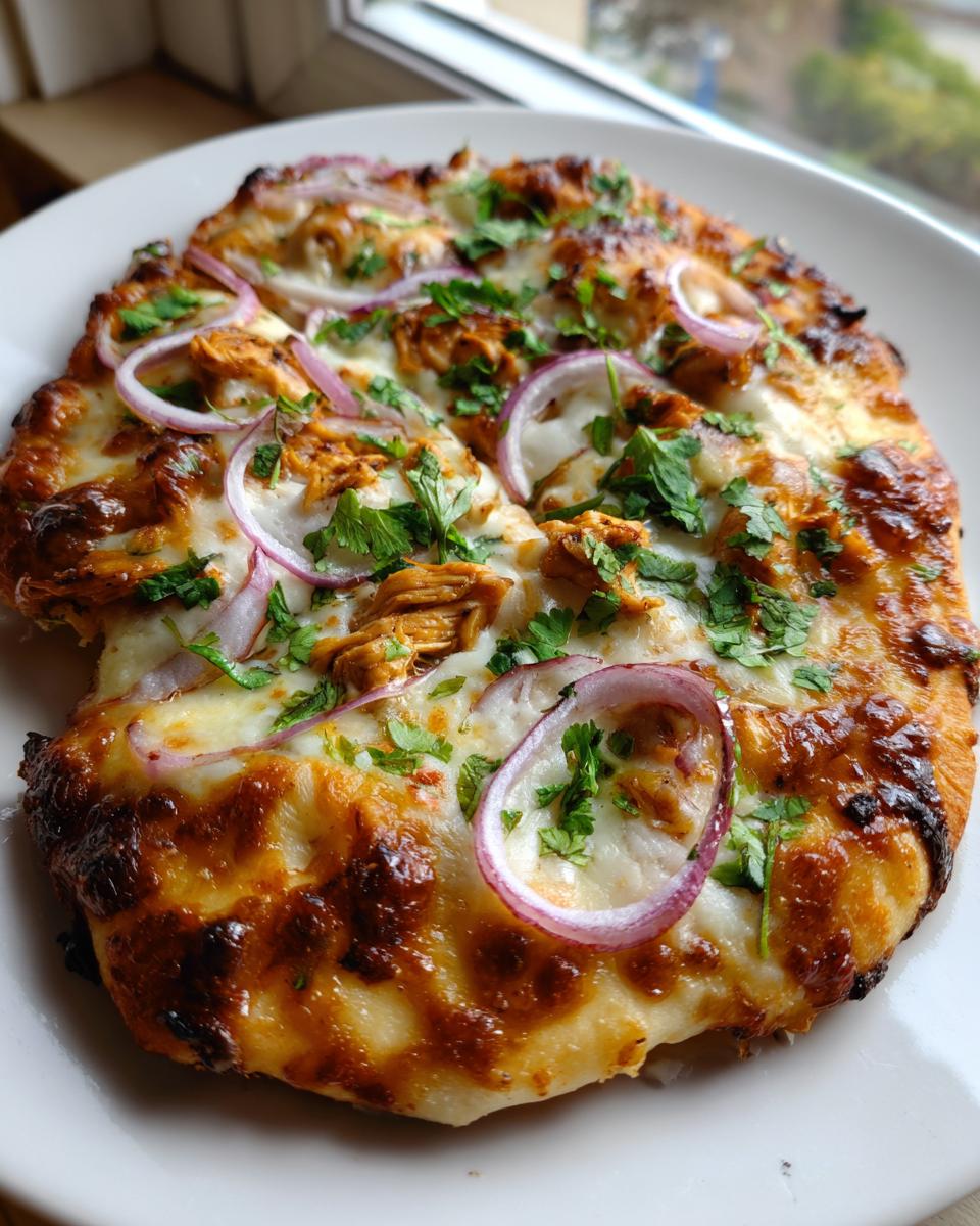 Close-up of a freshly baked Bbq Chicken Flatbread topped with melted cheese, red onion rings, and fresh cilantro.