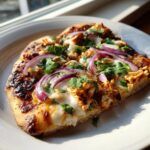 A close-up slice of Bbq Chicken Flatbread topped with melted cheese, red onion, and fresh cilantro.