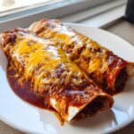 Two delicious Beef And Cheese Enchiladas smothered in red sauce and melted cheddar cheese, served on a white plate.