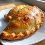Close-up of two golden-brown Beef Empanadas With Flaky Crust resting on a white plate.