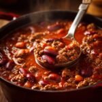A ladle scooping up rich, steaming Best Classic Beef Chili filled with ground beef and kidney beans.