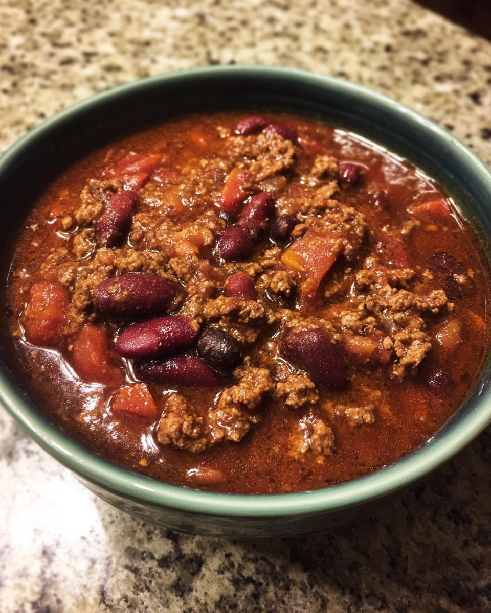 Close-up of a teal bowl filled with rich, hearty Best Slow Cooker Chili featuring ground beef and kidney beans.