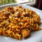 A close-up of creamy Cajun Chicken Pasta featuring rotini noodles coated in a rich, orange sauce with chunks of chicken and parsley.