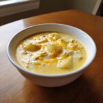 A white bowl filled with creamy, yellow Cheeseburger Soup featuring chunks of potato and melted cheddar cheese.