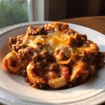 A portion of cheesy Beef Enchilada Tortellini bake served on a white plate, covered in melted cheddar and mozzarella.