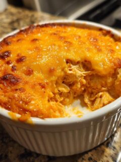 A close-up view of hot, cheesy Buffalo Chicken Dip served in a small white ramekin, showing shredded chicken texture.